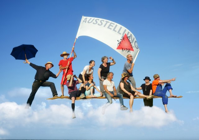 Fotomontage des KunstWerkWege-Teams auf einem fliegenden Teppich hoch im Himmel mit großem weißem Banner mit dem Text „KunstWerkWege“ und dem Logo.