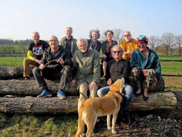 Das KunstWerkWege-Team sitzt auf längs liegenden Baumstämmen, im Vordergrund ein rotbrauner Hund.